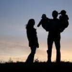 family with children on hands, sunset sky