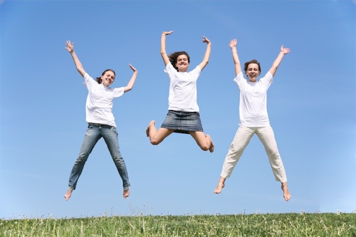 Three girlfriends in white T-shorts jump having waved hands