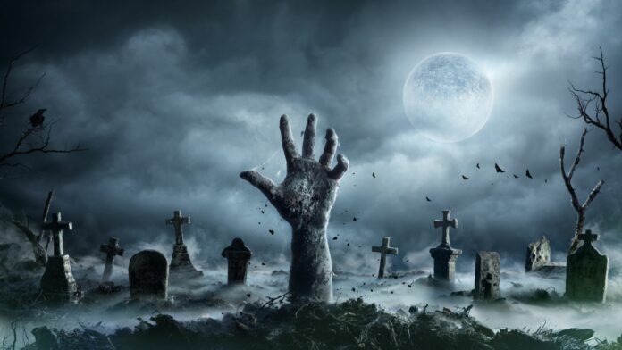 Eine Hand streckt sich aus dem Boden auf einem Friedhof bei Nacht