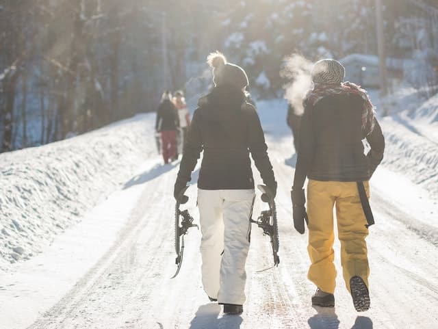 Menschen auf einem verschneiten Weg tragen Skier